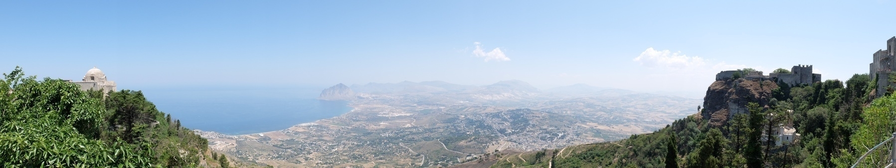 Vue panoramique d'un paysage côtier avec des collines, la mer et des bâtiments anciens au sommet.