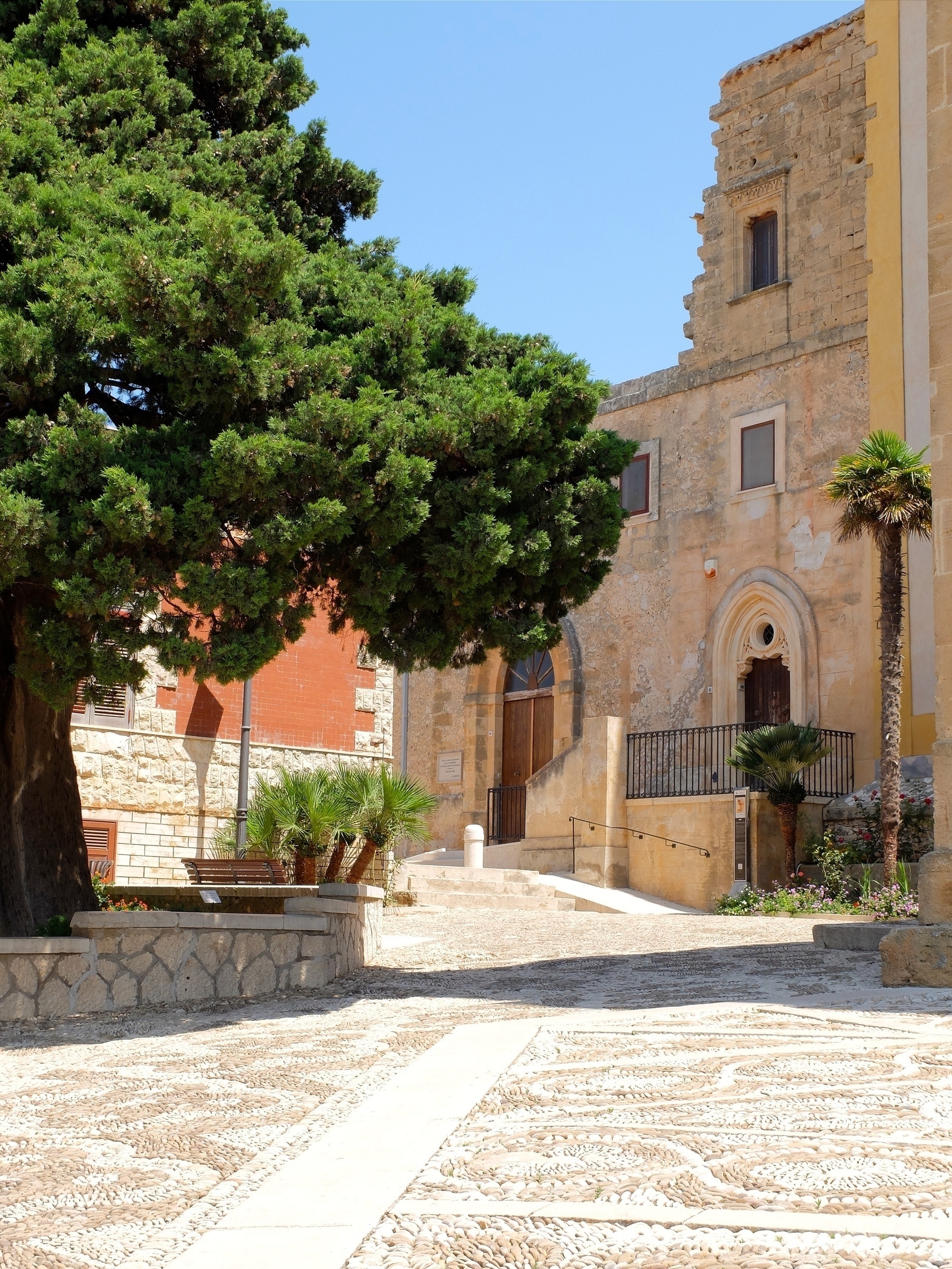 Un arbre se tient à côté d'un bâtiment historique en pierre sous un ciel bleu.