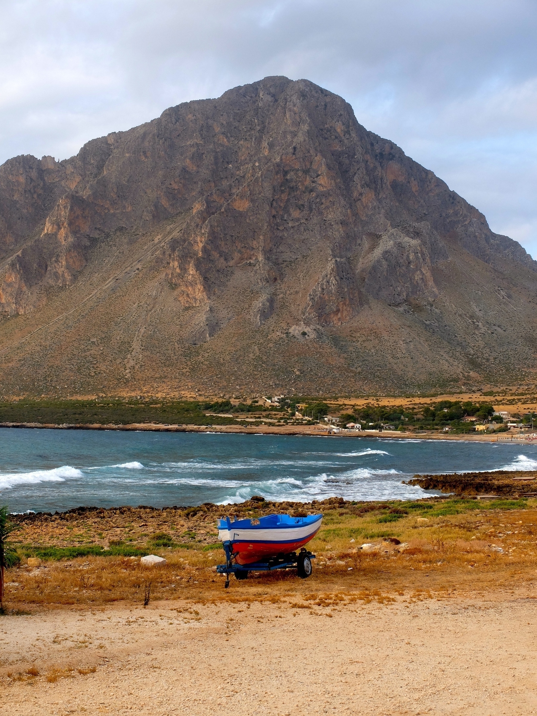 Une petite barque bleue et rouge est posée sur une remorque devant un paysage de montagne imposante près de l'eau.