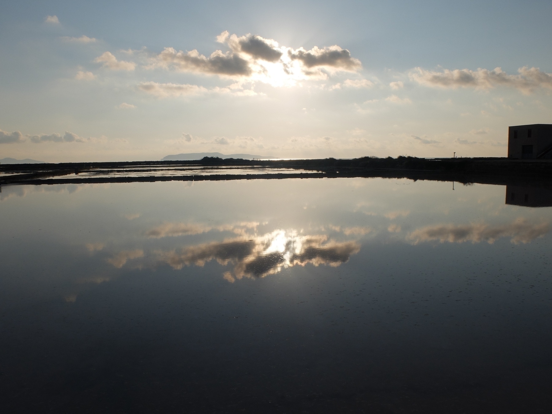 Un paysage paisible montre le reflet des nuages et du soleil couchant sur une grande étendue d'eau calme.