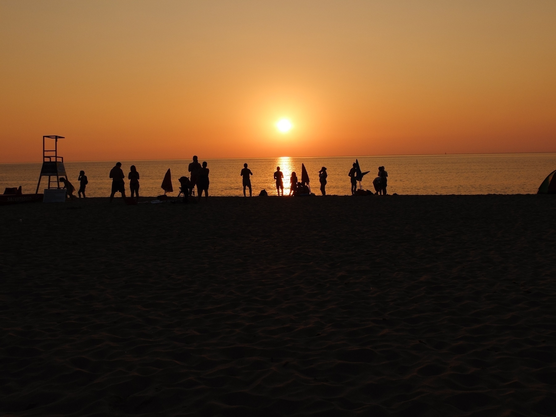 Des personnes se tiennent sur une plage, regardant un coucher de soleil vibrant au-dessus de l'océan.