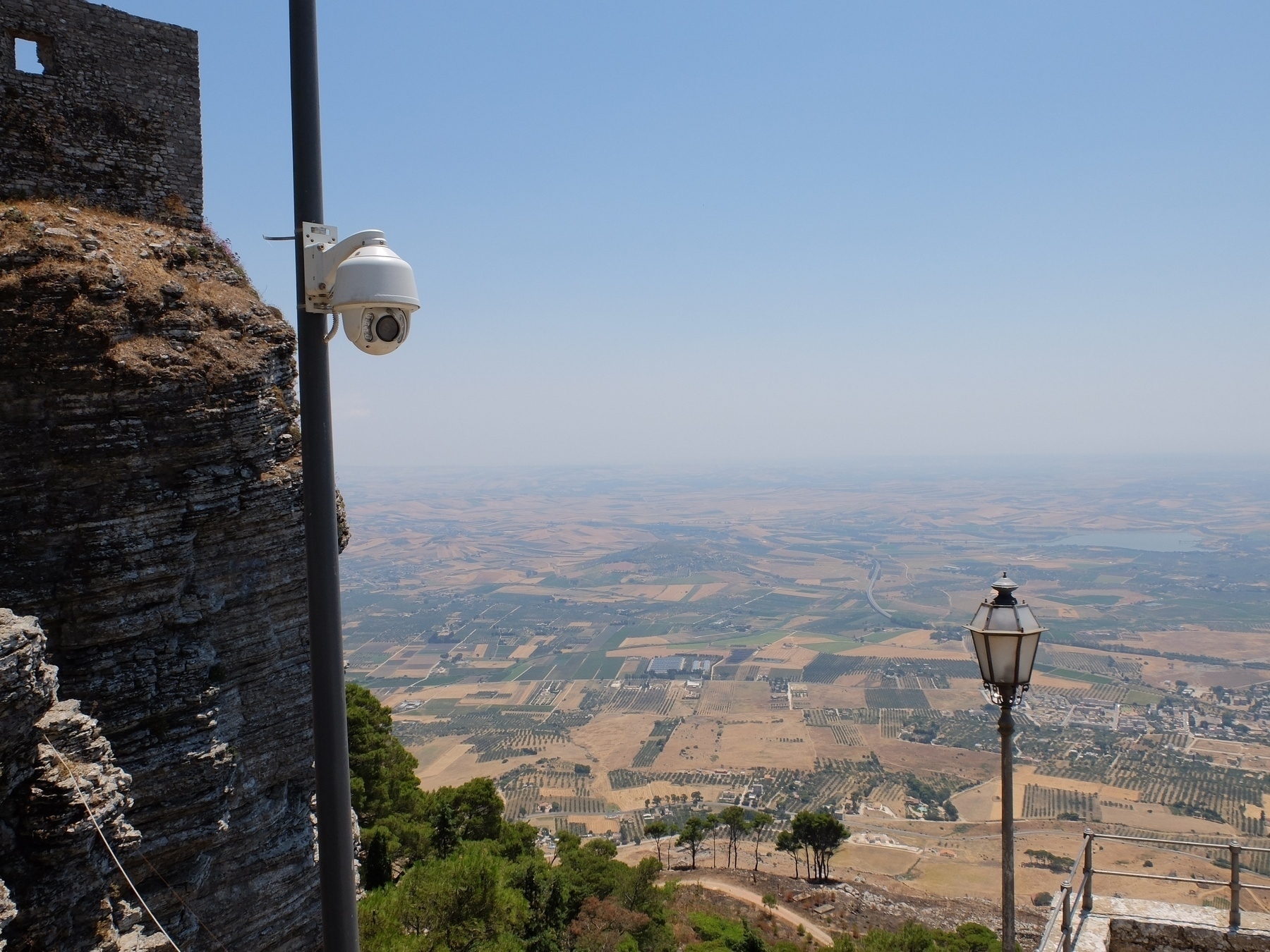 Une caméra de surveillance et un lampadaire surplombent un vaste paysage rural vu depuis un fort.
